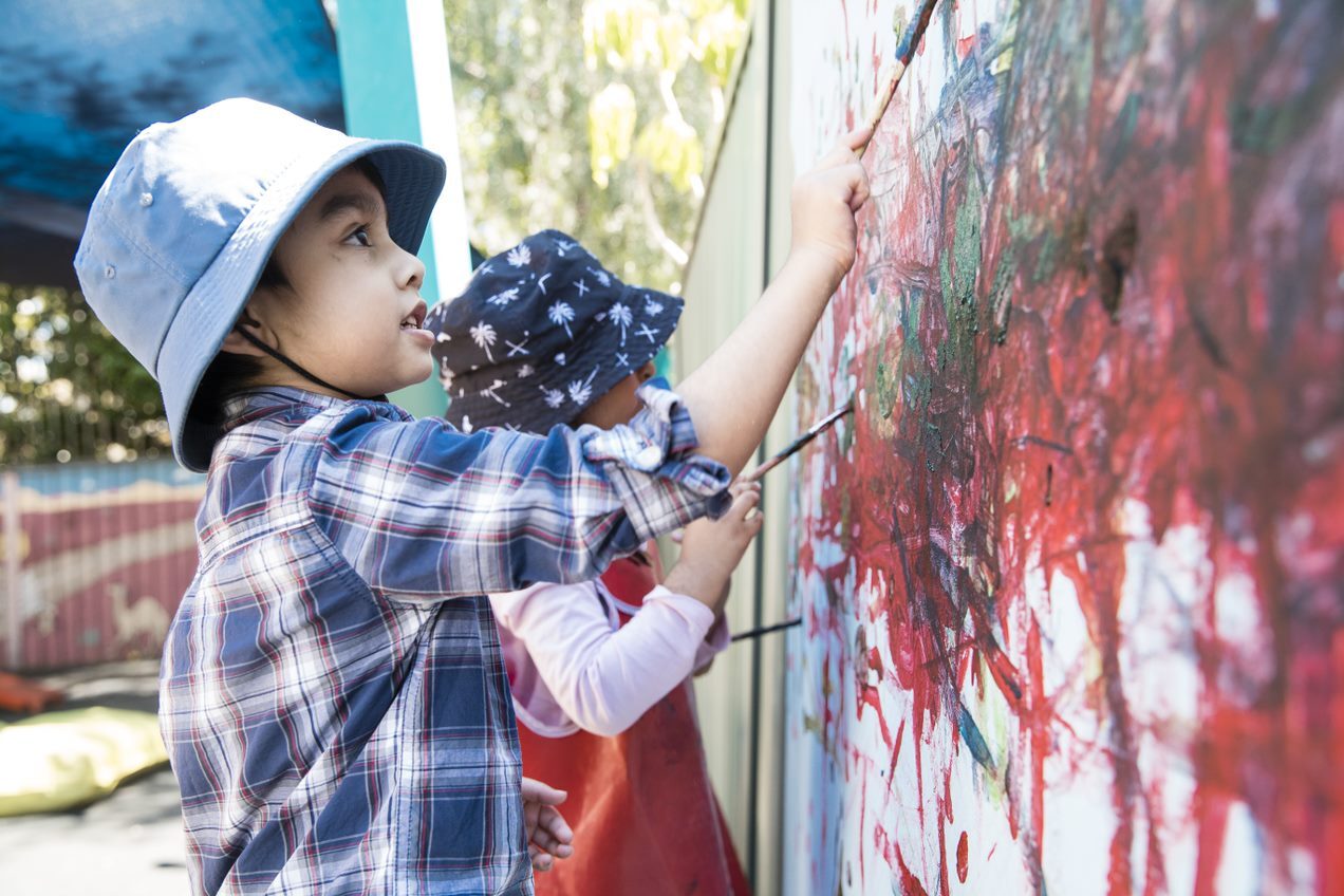Two young children painting on a wall