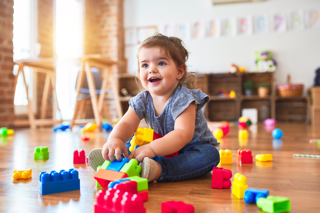 Beautiful toddler sitting on the floor playing with building blocks toys at kindergarten